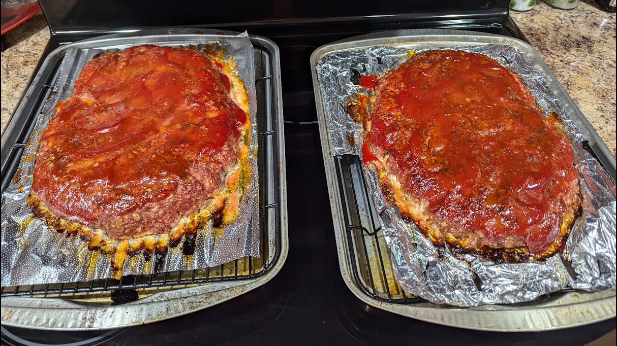 Two finished smoked meatloaves glazed with ketchup on foil-lined pans