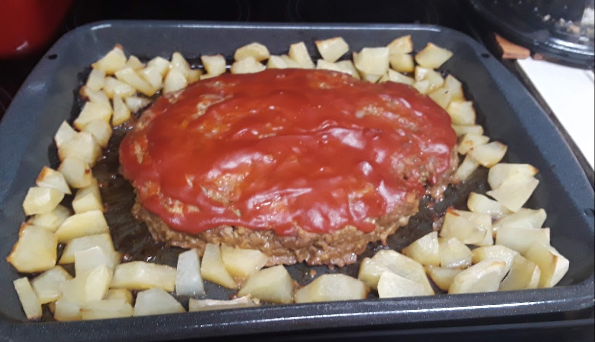 Meatloaf glazed with ketchup and surrounded by roasted potatoes in an oven pan